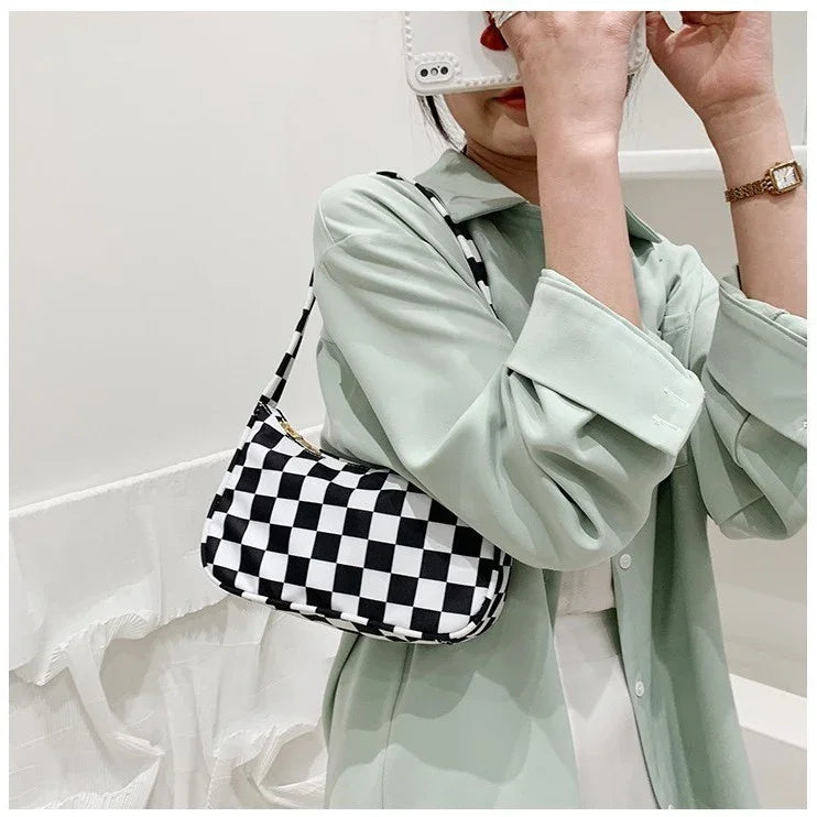 Woman wearing pastel green jacket holding phone, carrying black and white checkered shoulder bag
