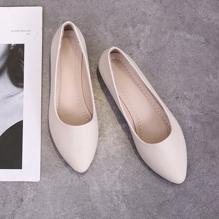 Pair of beige pointed-toe flat shoes on gray concrete floor next to black and white magazine