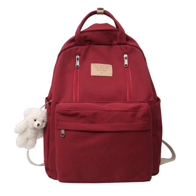 Maroon backpack with front zipper pockets and a small white teddy bear keychain attached