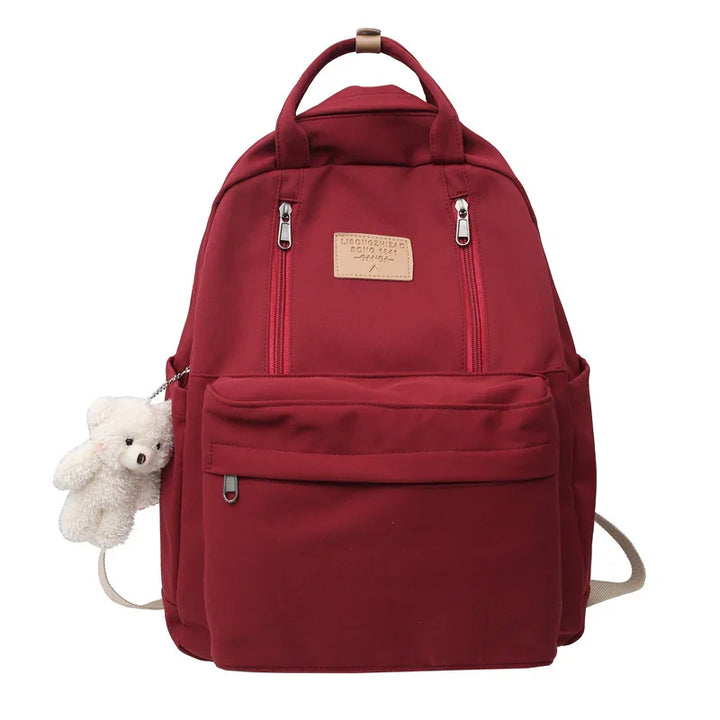 Maroon backpack with front zipper pockets and a small white teddy bear keychain attached