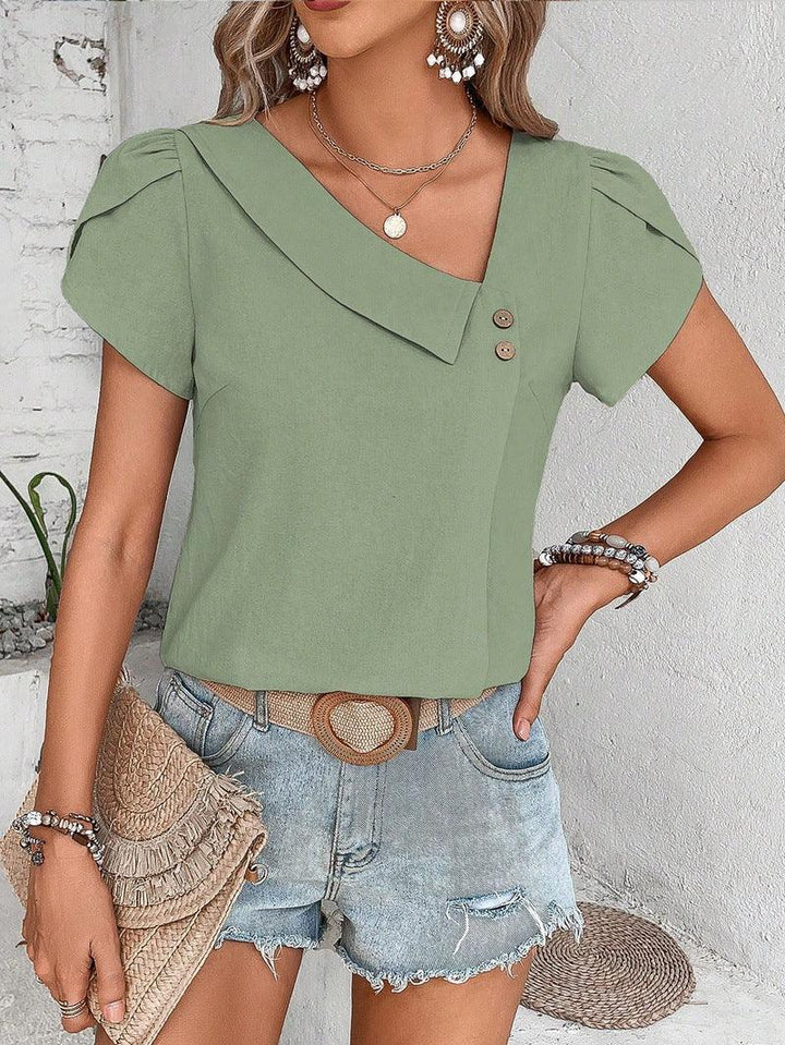 Woman wearing green asymmetric blouse with buttons and light denim shorts, accessorized with earrings and bracelets