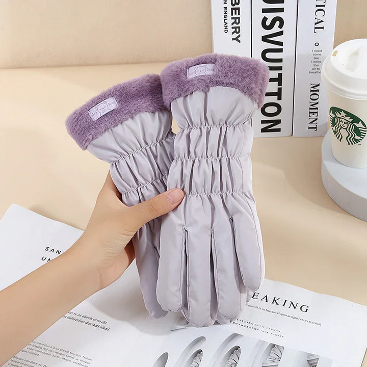 Hand holding light gray winter gloves with purple fuzzy cuffs, stylish warm gloves on table with books and Starbucks cup