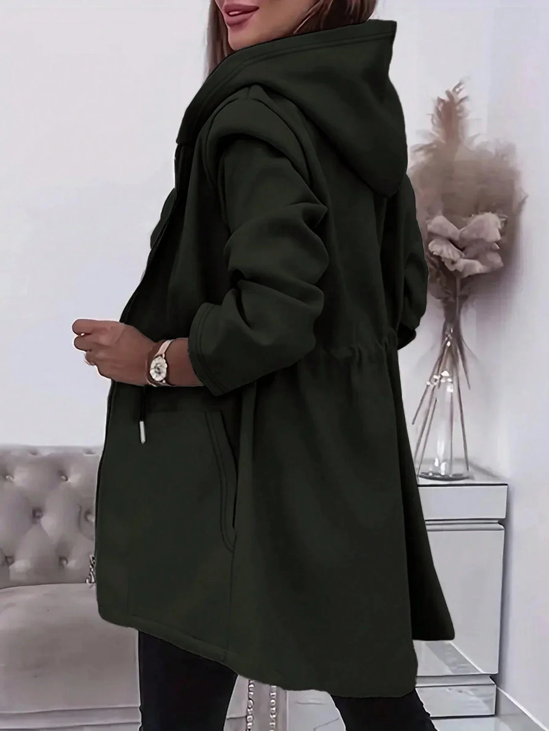 Woman wearing a dark green hooded jacket with pockets in a modern living room