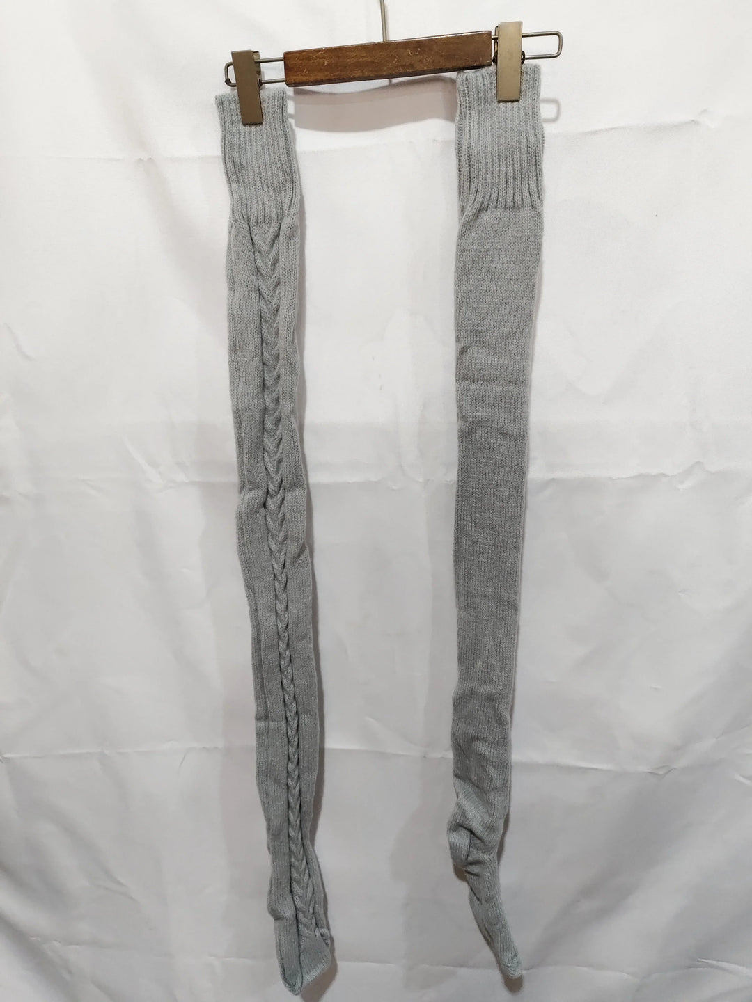 Pair of long grey knit socks hanging on wooden hanger against white background