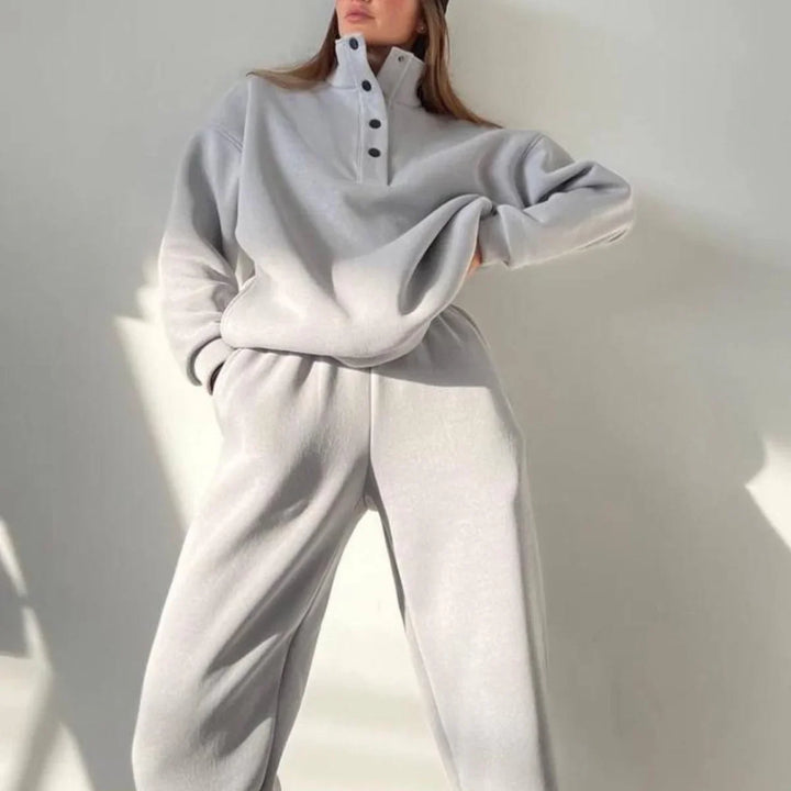Woman wearing light gray buttoned pullover and matching sweatpants in a minimal indoor setting