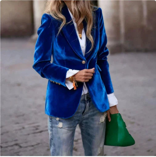 Woman wearing a royal blue velvet blazer, white shirt, distressed jeans, and holding a green handbag
