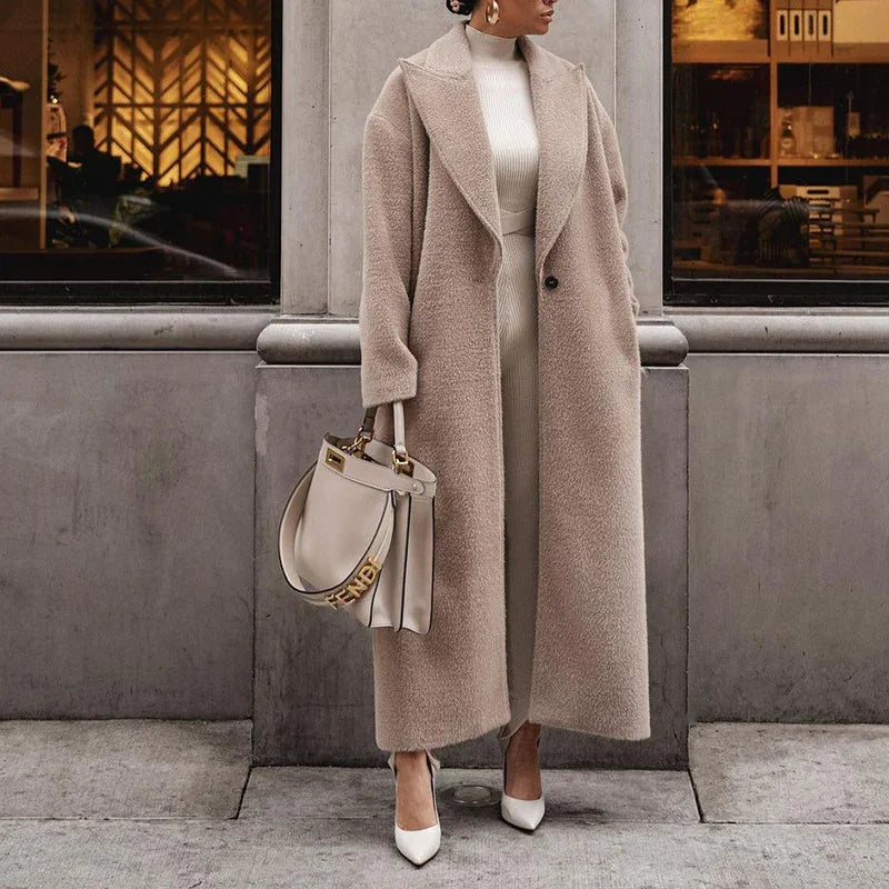 Woman wearing long beige teddy coat, cream knit dress, white heels, holding beige Fendi handbag on city sidewalk