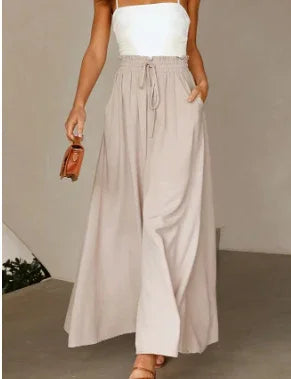 Woman wearing high-waisted beige wide-leg pants with pockets and a white sleeveless top holding a small brown handbag
