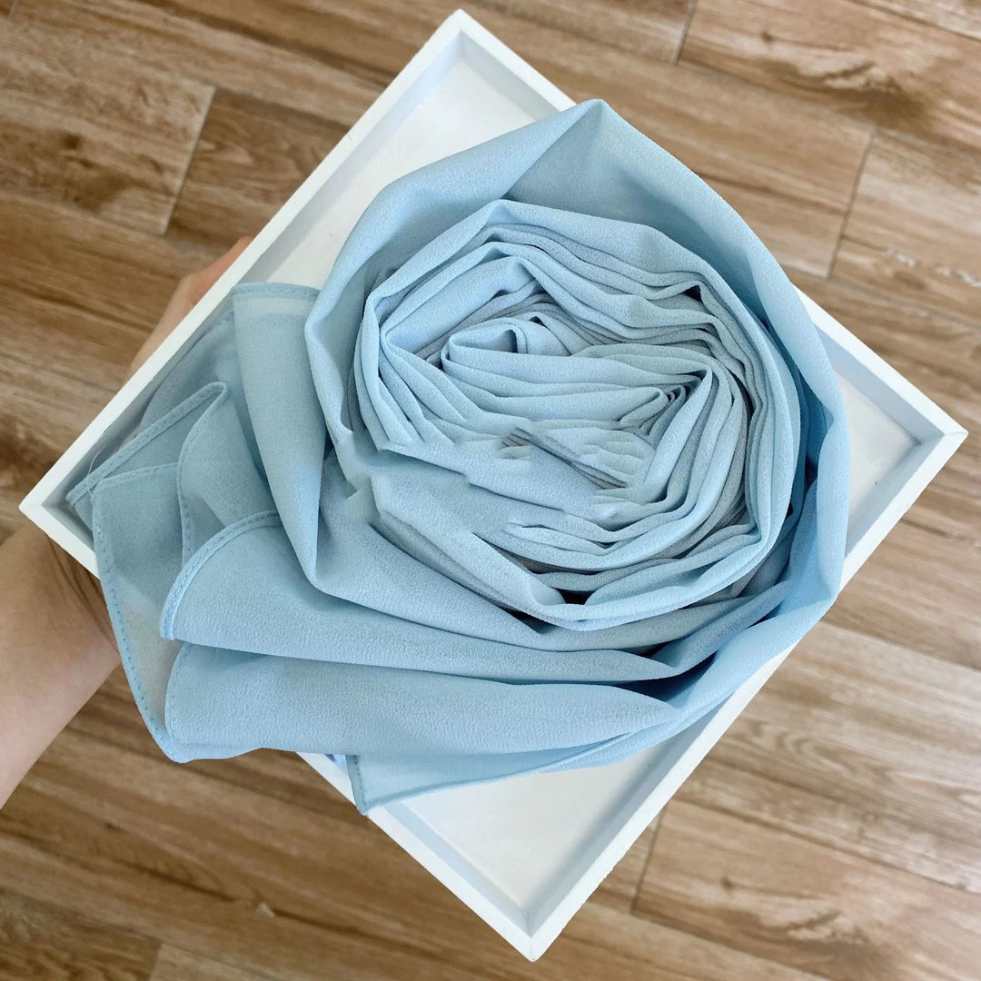 Hand holding white tray with neatly rolled soft light blue fabric on wood floor