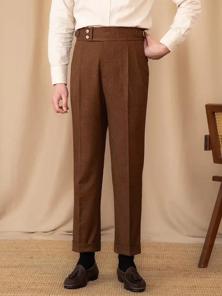 Man wearing brown high-waisted tailored trousers with button details, black socks, and dark tassel loafers