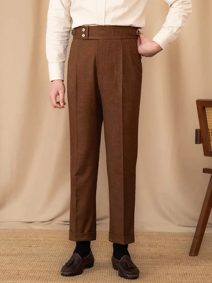 Man wearing brown high-waisted tailored trousers with button details, black socks, and dark tassel loafers