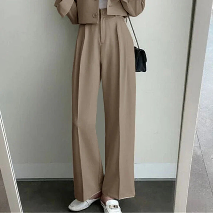 Women wearing beige wide-leg trousers with white loafers and black shoulder bag in minimal indoor setting