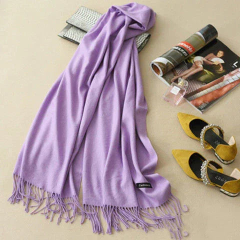 Soft lavender cashmere scarf with fringes laid out with yellow jeweled heels, silver clutch, perfume, and fashion magazines