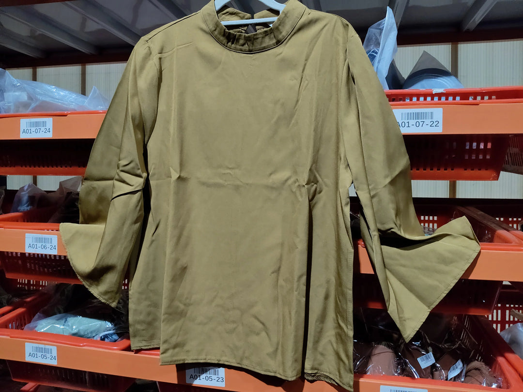 Beige long sleeve blouse with flared cuffs hanging in front of orange plastic storage bins in a warehouse