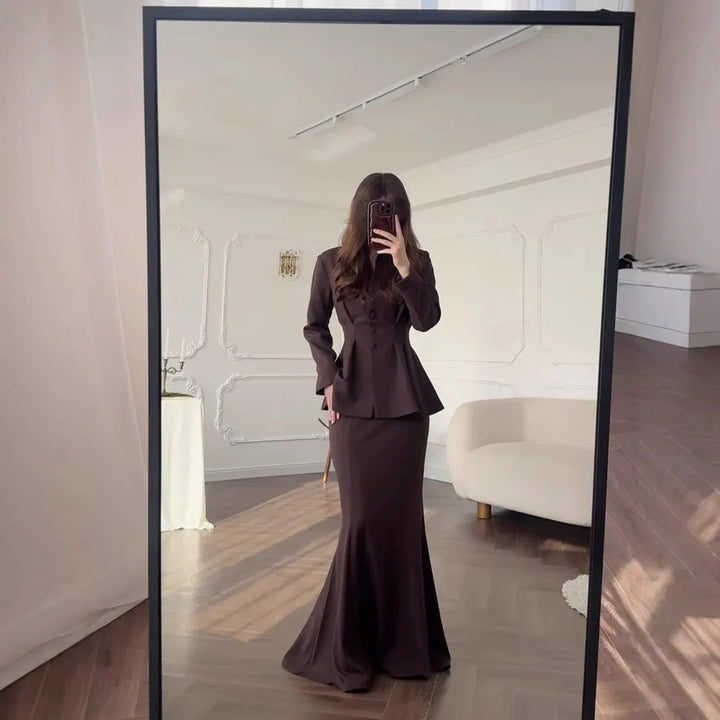 Woman wearing a fitted dark brown peplum blazer and matching long mermaid skirt in elegant room