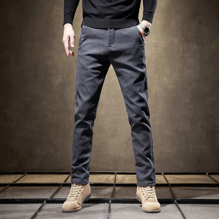 Man wearing dark gray slim-fit pants and beige suede boots standing on metal grid floor
