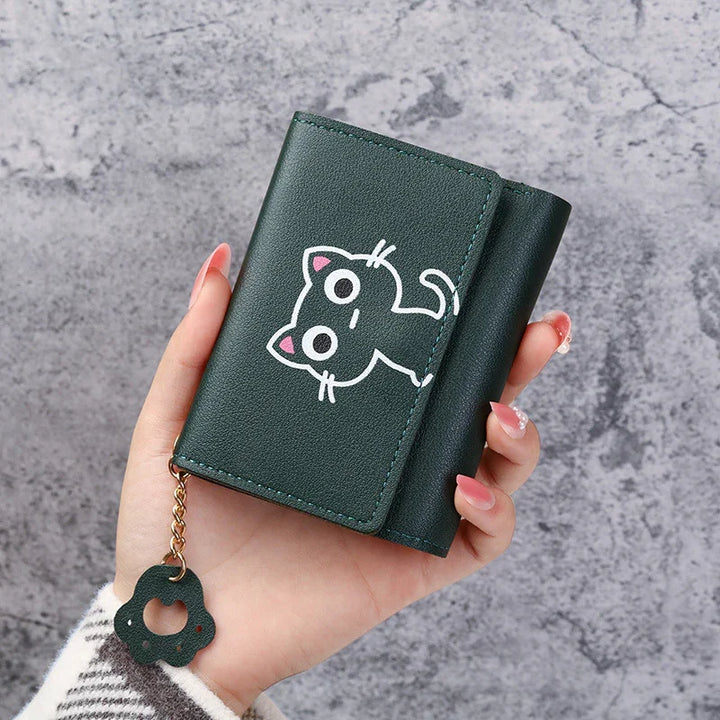 Hand holding dark green wallet with cute cartoon black cat and flower charm on chain