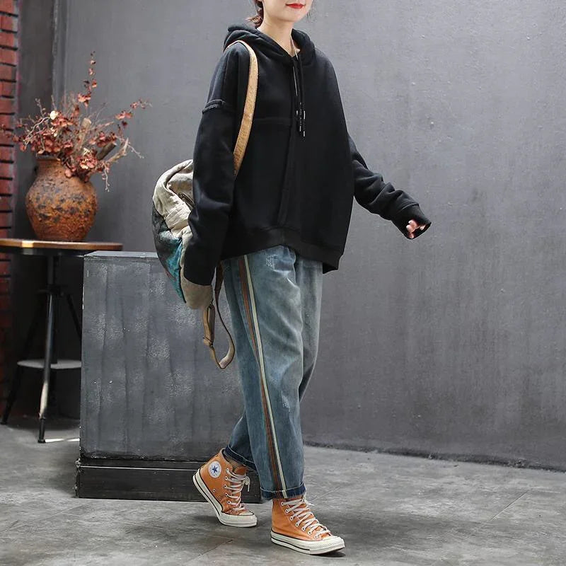 Person wearing black hoodie, blue jeans with side stripes, orange high-top sneakers, carrying a backpack indoors