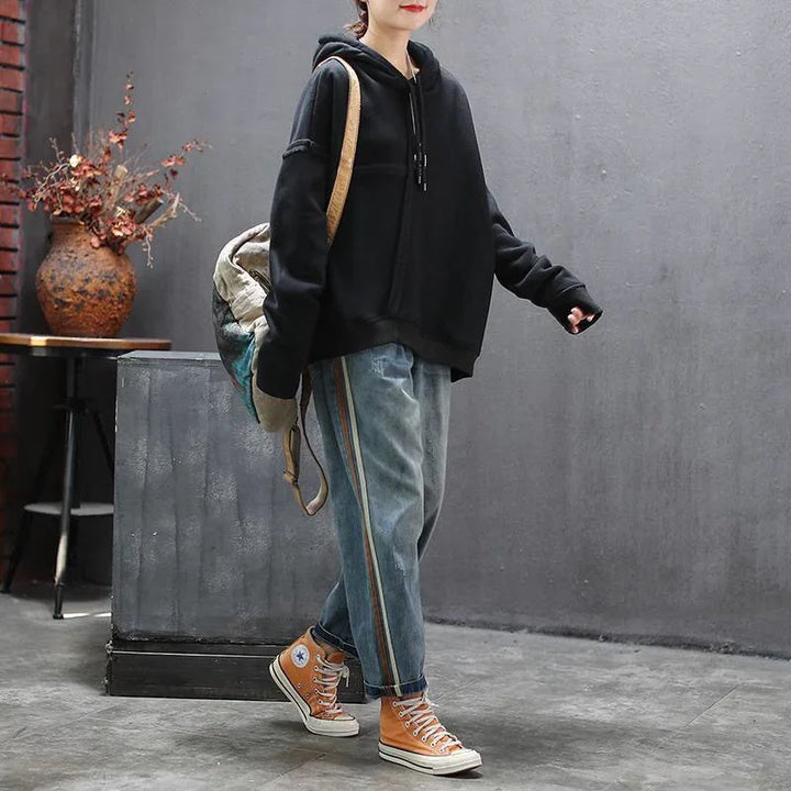 Person wearing black hoodie, blue jeans with side stripes, orange high-top sneakers, carrying a backpack indoors