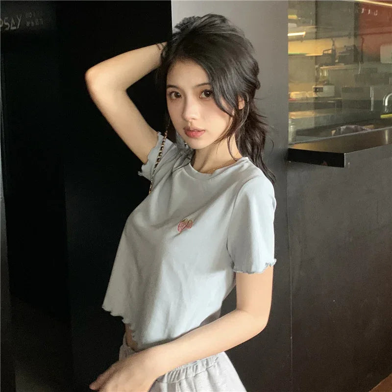 Young woman in light gray cropped t-shirt posing indoors with one arm raised, casual fashion style