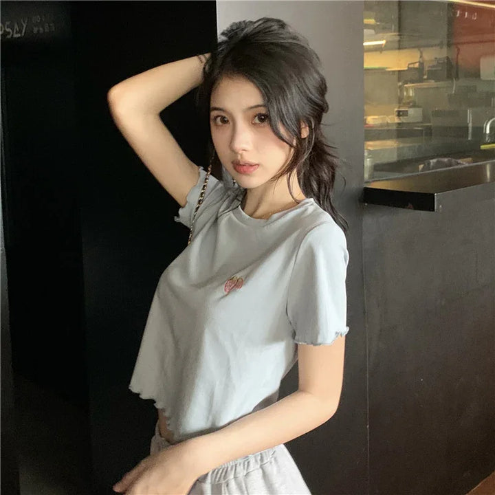 Young woman in light gray cropped t-shirt posing indoors with one arm raised, casual fashion style