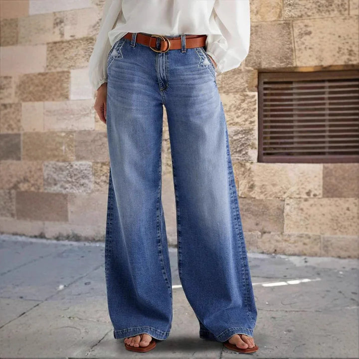 Woman wearing wide leg blue denim jeans with brown belt and white blouse standing on pavement