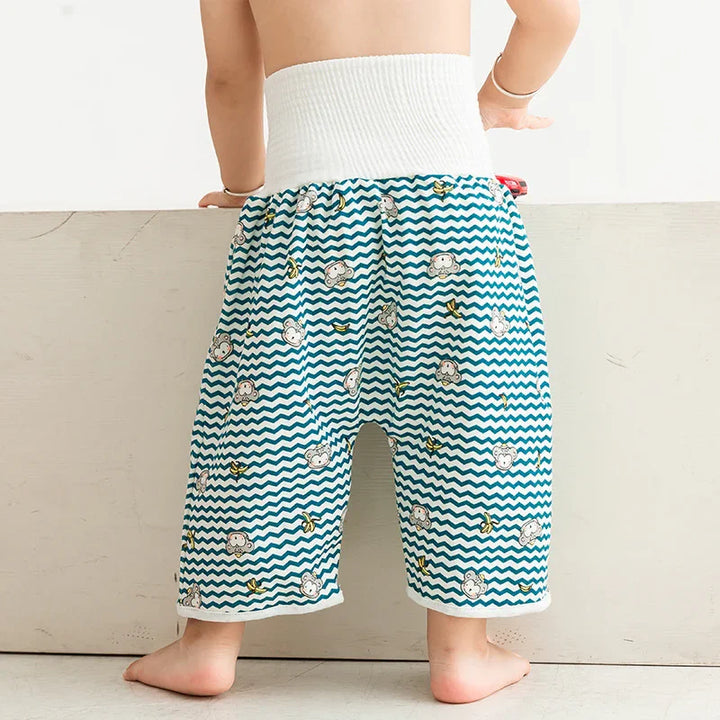 Toddler wearing loose blue chevron pants with monkey and banana prints, standing barefoot indoors