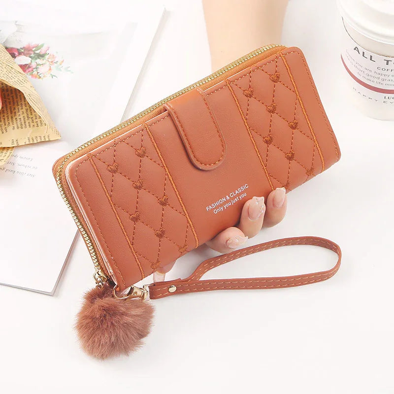 Brown quilted leather wristlet wallet with gold zipper and pom pom charm on white background