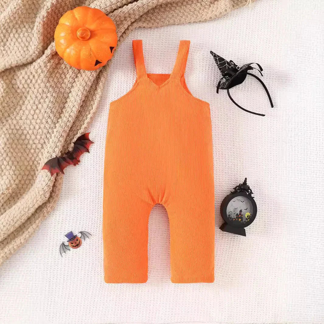 Orange baby romper with Halloween decorations including pumpkin, bat, witch hat headband, and spooky ornament on white textured background
