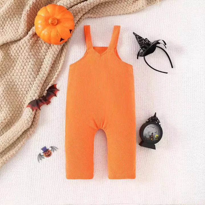 Orange baby romper with Halloween decorations including pumpkin, bat, witch hat headband, and spooky ornament on white textured background