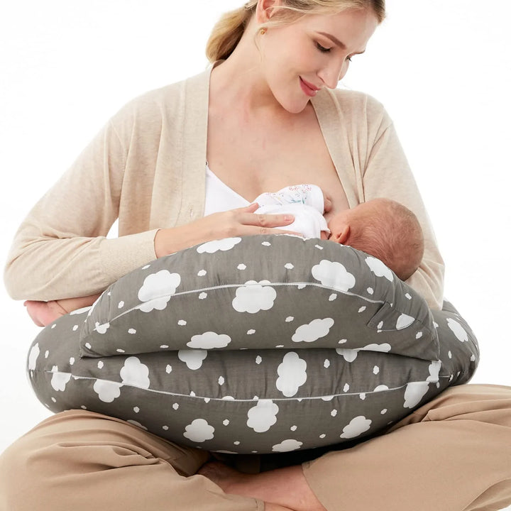 Mother breastfeeding baby using gray cloud-patterned nursing pillow sitting cross-legged