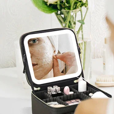 Woman with facial mask seen in a lighted mirror of an open black makeup and skincare organizer on a vanity table