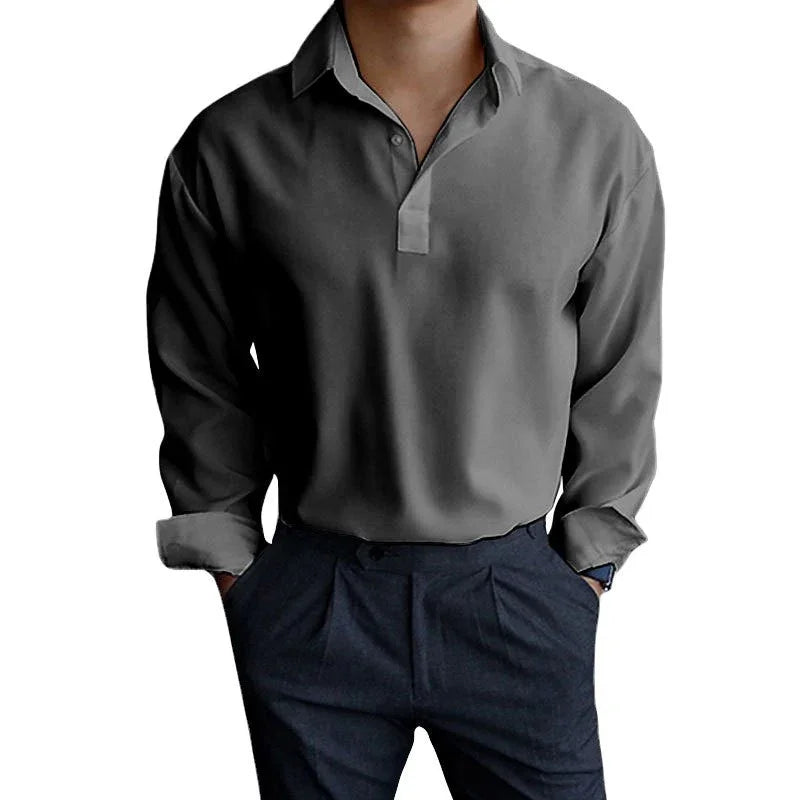 Man wearing a dark gray long-sleeve polo shirt and navy pleated trousers with hands in pockets