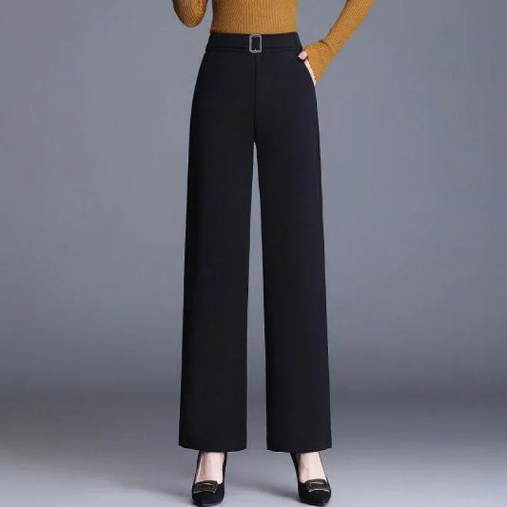 Woman wearing black wide-leg trousers with belt and black heels against gray background