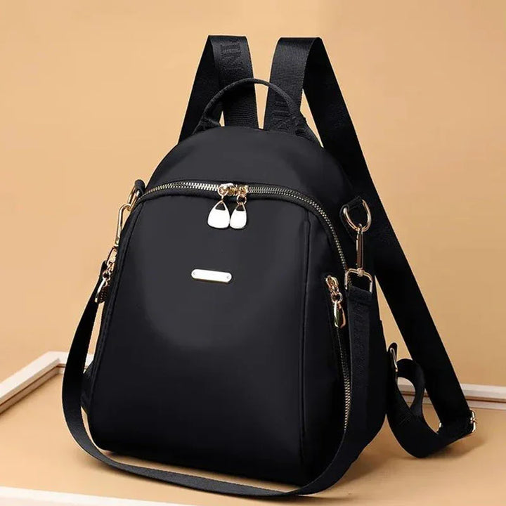 Black nylon backpack with gold zippers and adjustable straps on beige background