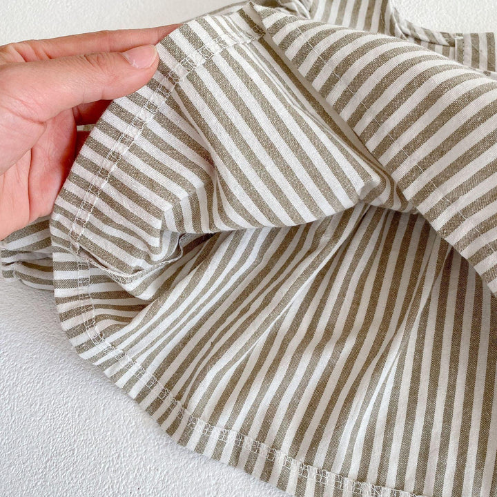 Hand holding beige and white striped cotton fabric with hem stitching detail on a white surface