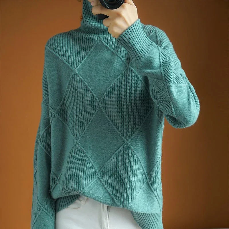 Person wearing teal green textured knit turtleneck sweater with diamond pattern, paired with white pants