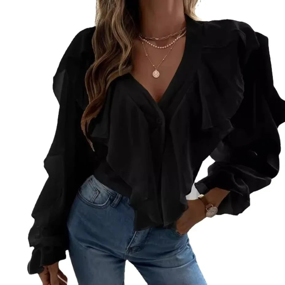 Woman wearing black ruffle blouse with long sleeves and blue jeans, accessorized with layered necklaces and watch
