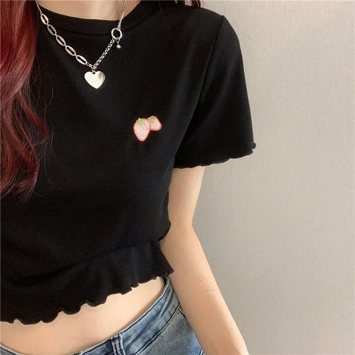 Woman wearing black cropped t-shirt with strawberry patch and silver heart necklace