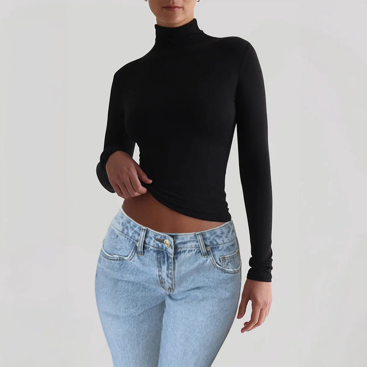 Woman wearing black long sleeve turtleneck top and light blue high-waisted jeans on plain background