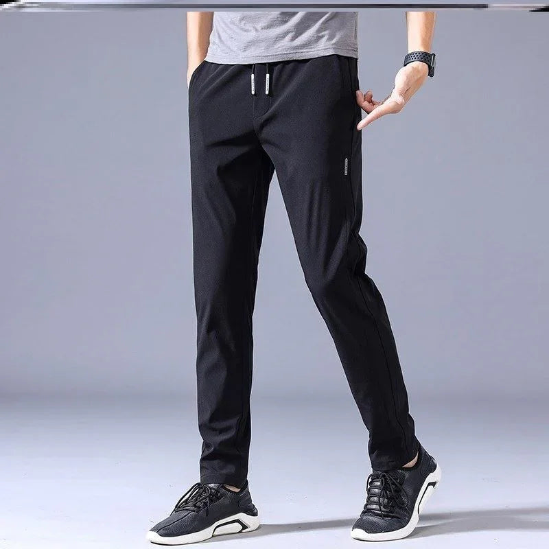 Man wearing black casual jogger pants with drawstring and black sneakers on gray background