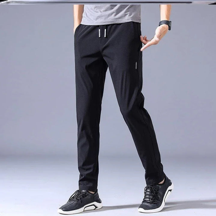 Man wearing black casual jogger pants with drawstring and black sneakers on gray background