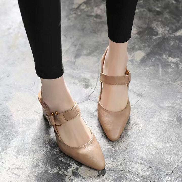 Beige pointed toe flat shoes with strap and decorative bead on concrete floor, worn with black pants