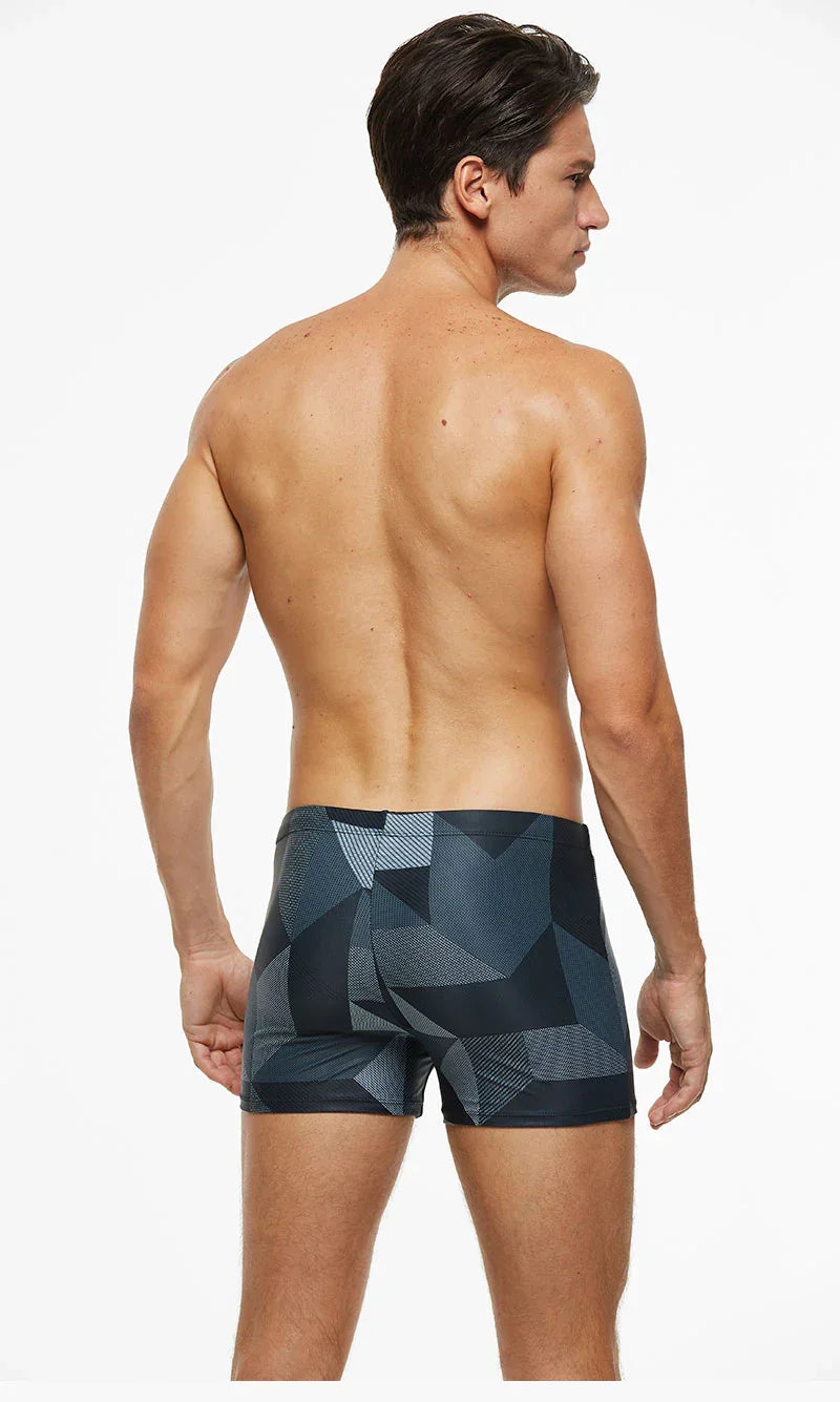 Rear view of shirtless man wearing black and gray geometric patterned swim trunks on white background