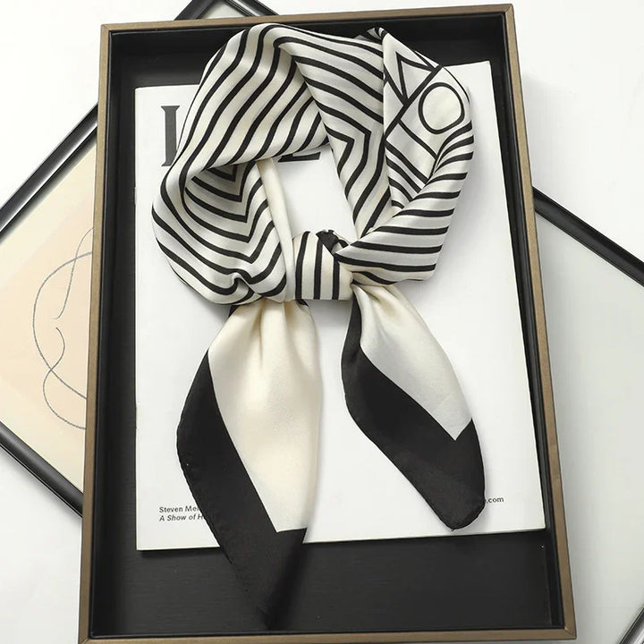Black and white striped silk scarf with geometric pattern displayed on a black tray with magazines