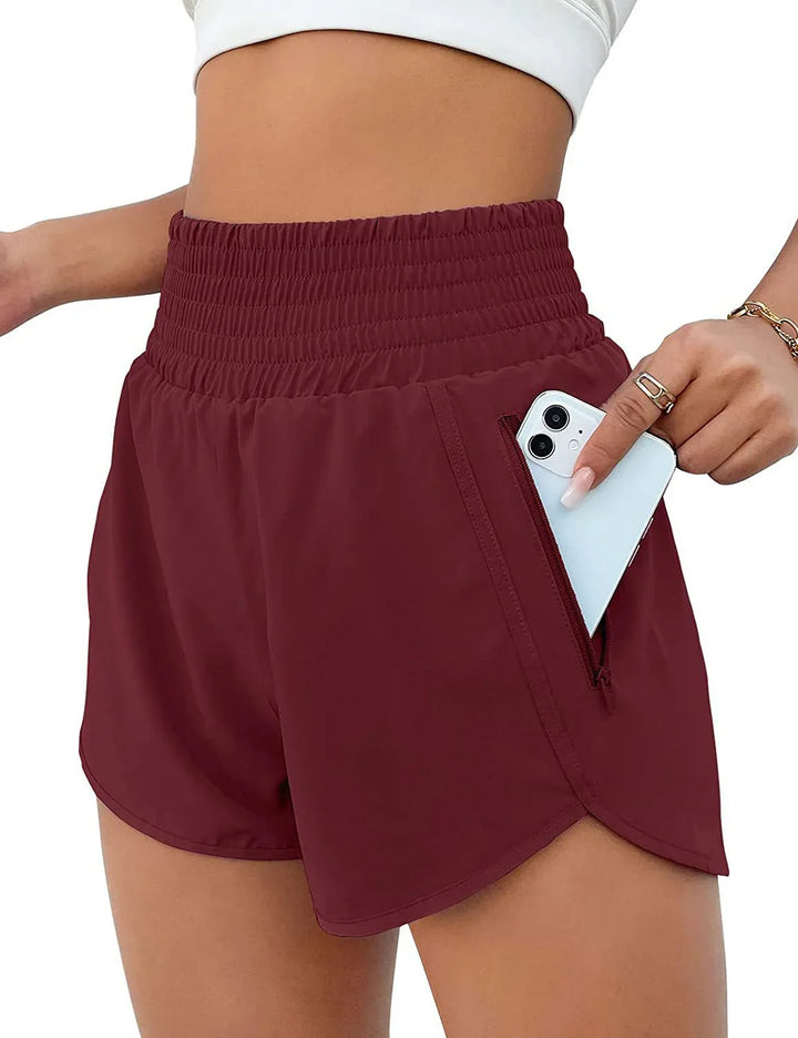Close-up of woman wearing maroon athletic shorts with high waist and zippered pocket holding a smartphone