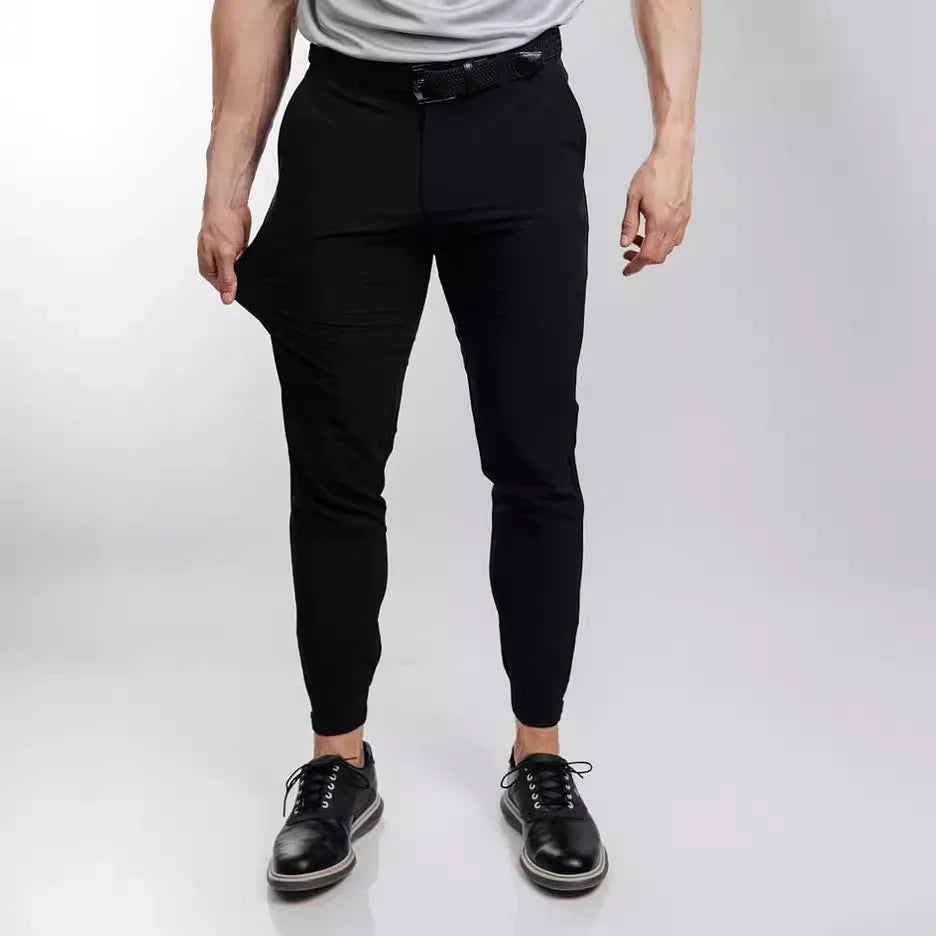 Man wearing slim-fit black stretch pants pulling fabric to show flexibility, paired with black dress shoes