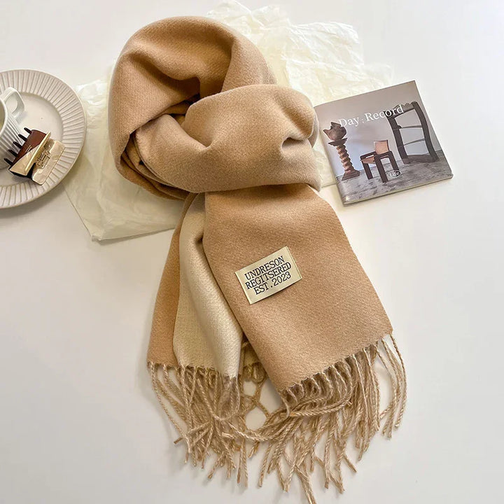 Beige and cream wool scarf with fringes and label, styled with a hair clip and small book on white surface