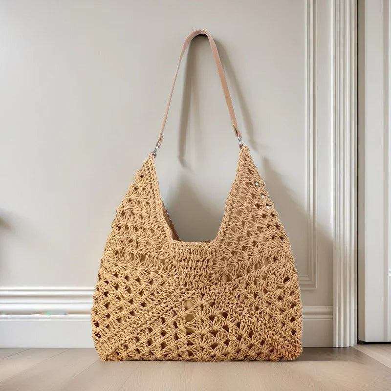 Beige crocheted handbag with leather strap hanging on white wall by wooden floor