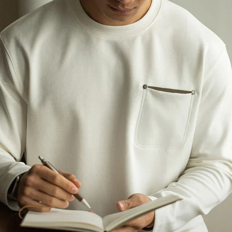 Man wearing white long sleeve shirt with front pocket, writing in notebook with pen